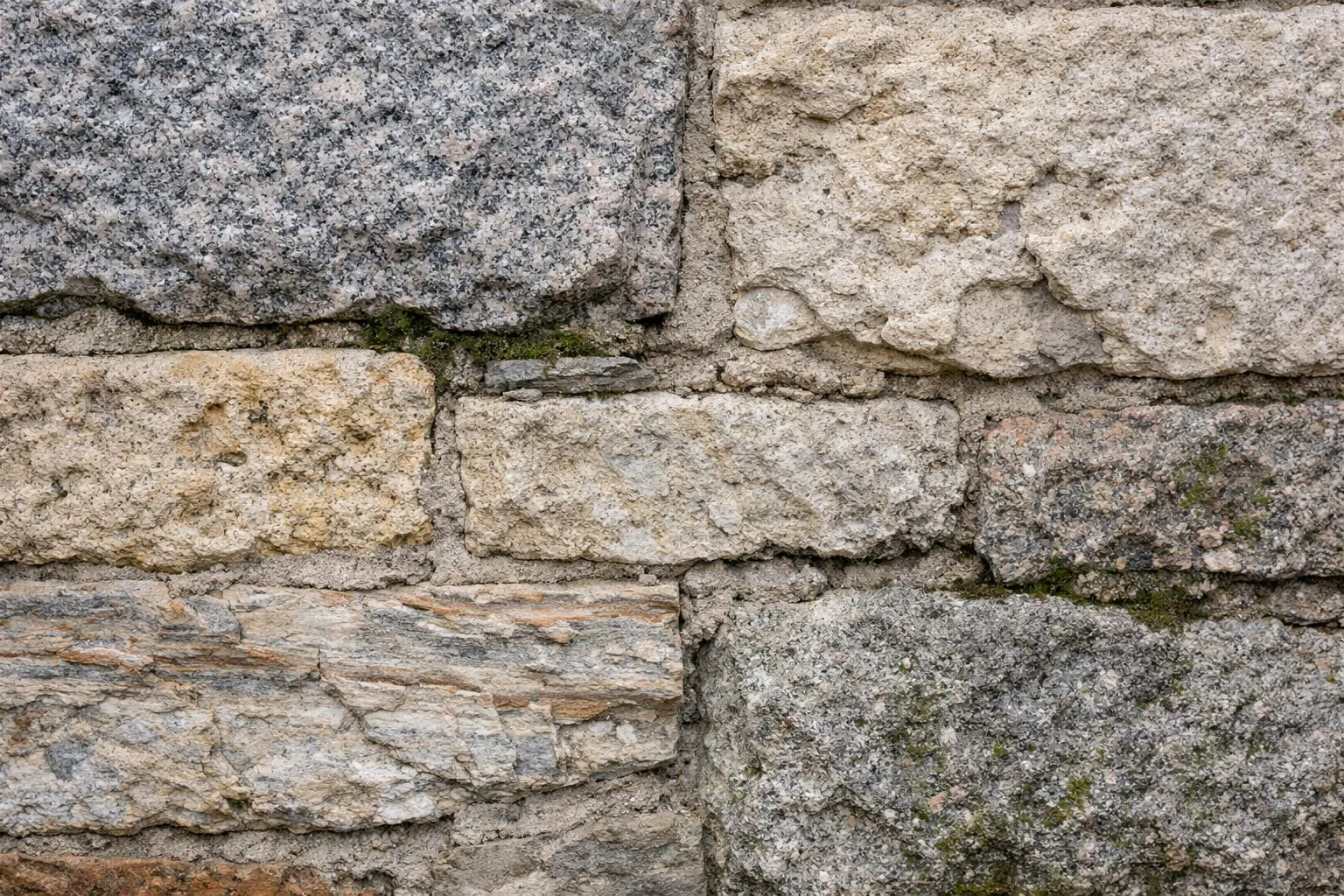 Mur de pierre grise et blanche avec des fissures et de la mousse.