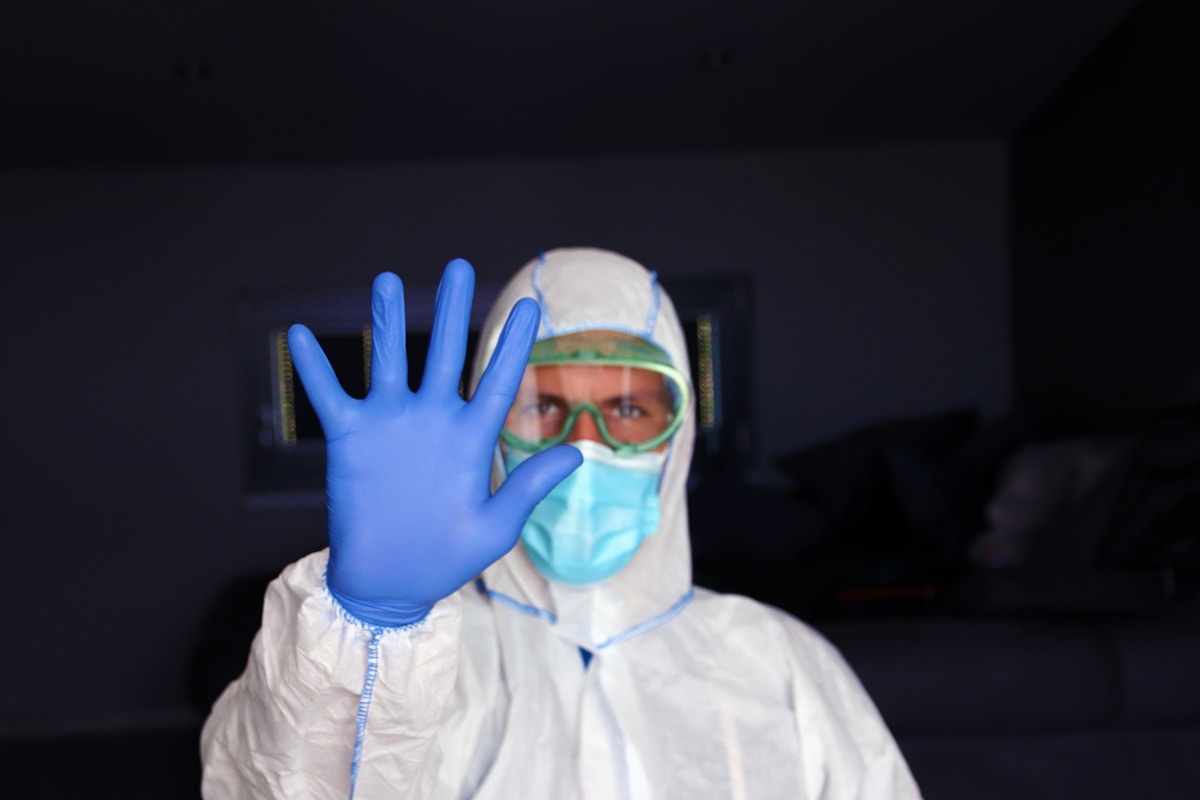 Personne en tenue de protection médicale faisant un geste d'arrêt.