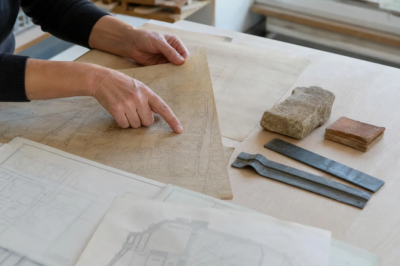 Mains d'un artisan examinant des plans architecturaux et des outils de construction.