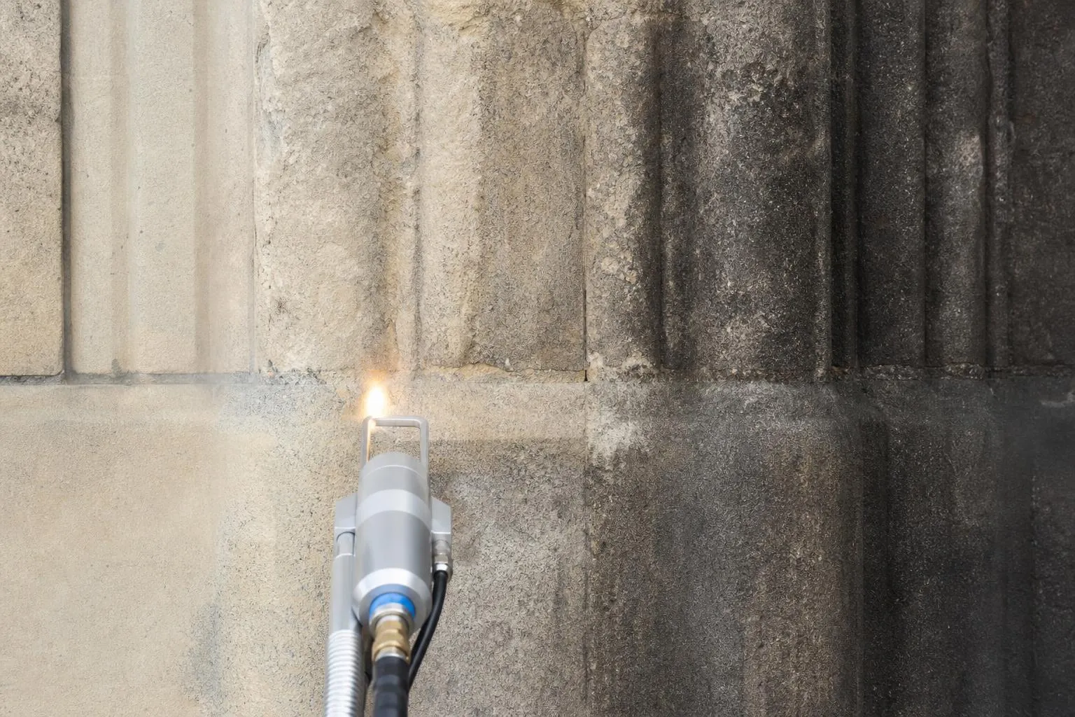 Tuyau de gaz propane allumé contre un mur de pierre rugueux.